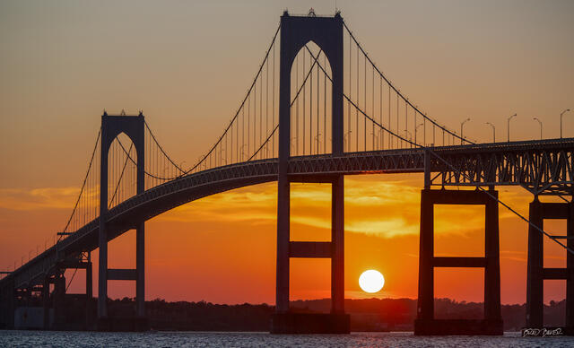 Newport Bridge silhouette in Rhode Island with the setting sun glowing between its towers over the bay