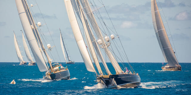 Fleet of magnificent sailing superyachts racing in close formation on sparkling blue Caribbean waters under sunny skies.