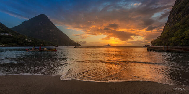 Panoramic golden sunset behind the Pitons in Sugar Beach St. Lucia with local fishermen rowing in a colorful wooden boat
