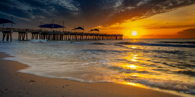 Sunrise over Pompano Beach Pier with waves washing onto the sandy shore