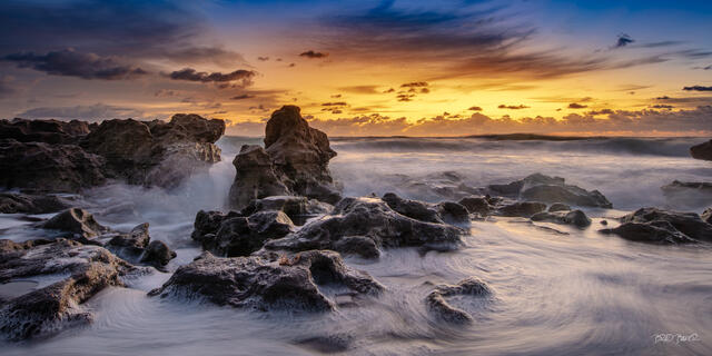Sunrise over rocky Jupiter Island Florida coastline with waves swirling around dark coral rocks, vivid orange and blue sky