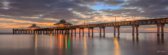 Fishing pier at Fort Myers Beach Florida stretching over calm ocean at sunset, glowing orange sky with soft clouds reflected in the water