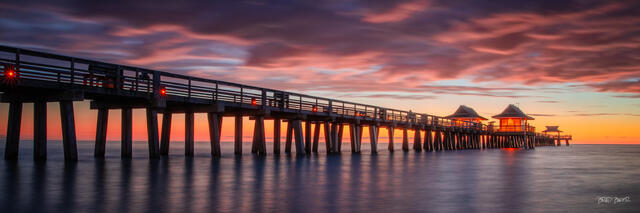 Panorama of a wooden pier at Naples Florida stretching into the ocean beneath a dramatic pink and purple sunset sky, calm water below