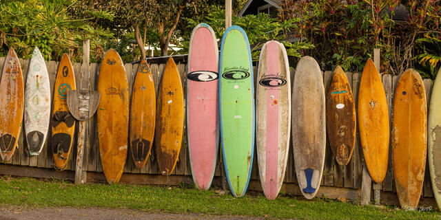 Row of sun-bleached vintage surfboards displayed along a wooden fence in Maui Hawaii.