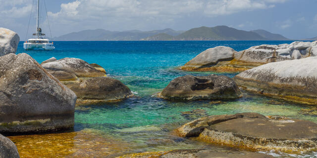 Turquoise Caribbean water surrounding smooth granite boulders with a catamaran offshore at The Baths Virgin Gorda BVI