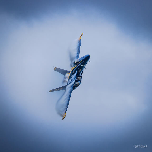 Blue Angels F/A-18 fighter jet banking sharply against clouds, wings streaked with vapor trails at Fort Lauderdale Air and Sea Show
