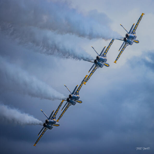 Four Blue Angels jets flying in tight diagonal formation with white smoke trails against a stormy sky at Fort Lauderdale Air and Sea Show