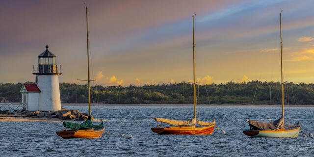 Small wooden sailboats moored near the Brant Point Lighthouse in Nantucket at sunset