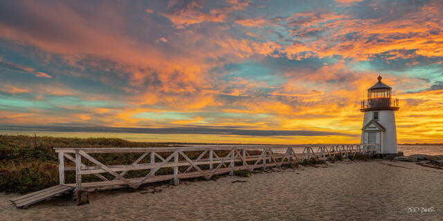 Weathered boardwalk leads across a beach toward Brant Point lighthouse Nantucket under a colorful sunrise sky