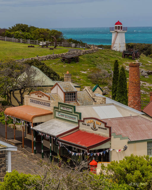Historic seaside village buildings and a red-roofed lighthouse overlook turquoise ocean waters in Victoria Australia