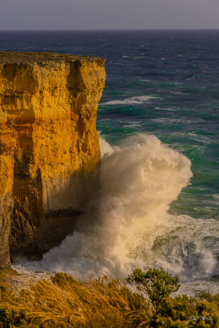 Powerful waves crashing against golden limestone cliffs along Australia's Great Ocean Road in the late afternoon sun