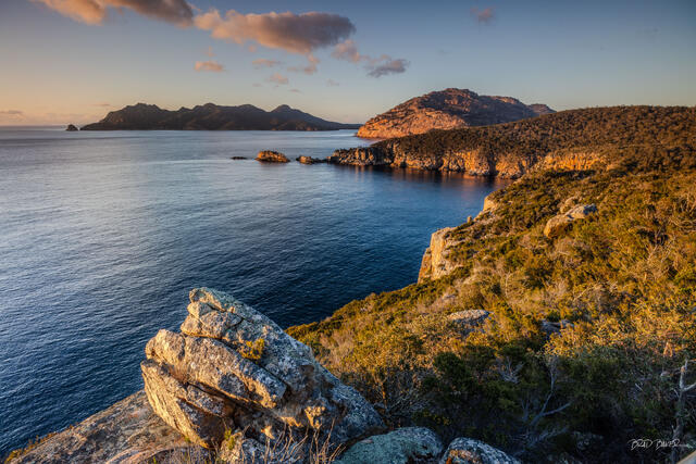 Rocky coastal cliffs and distant islands glowing in warm morning light at Cape Tourville , Tasmania