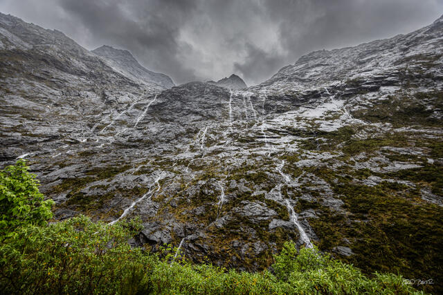 Dozens of thin waterfalls streaming down dark rain-soaked granite mountainside, Fiordland New Zealand
