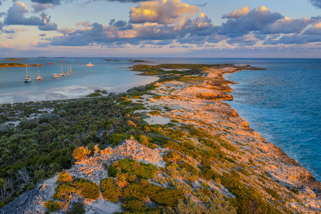 Sunset view of jagged limestone coastline with sailboats and calm turquoise waters under golden light at Warderick Wells Exumas