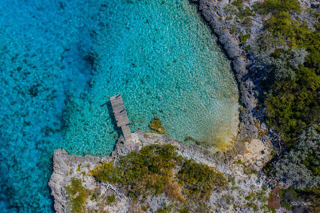 Aerial shot of turquoise bay through white sand and a wooden pier on a remote island at The Exumas