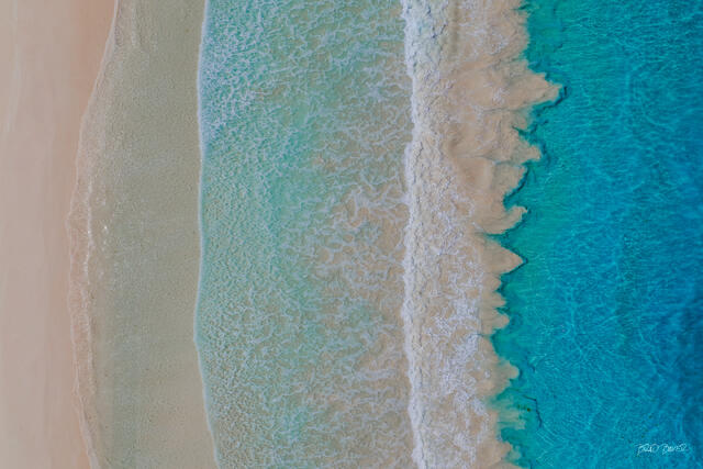 Overhead aerial view of gentle waves washing over Pink Sand beach between turquoise and deep blue ocean on Harbor Island Bahamas