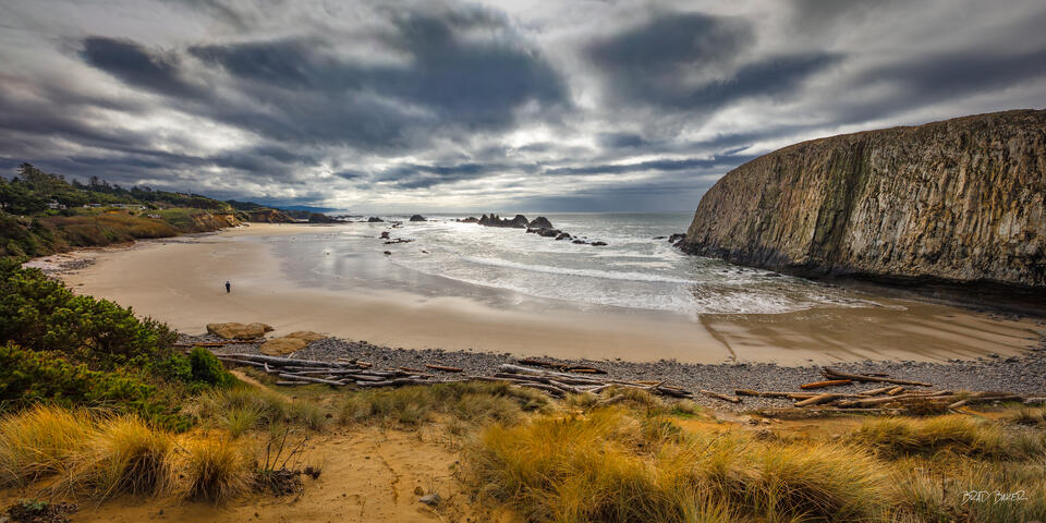 Misty coastal cove with dramatic clouds, sea stacks, and a lone figure on the beach at Seal Rocks Oregon