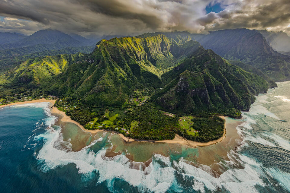 Aerial view of Kauai's Na Pali Coast with green cliffs, sandy beach, and crashing surf