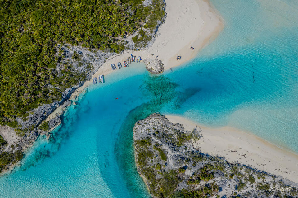 Aerial perspective of rocky limestone coves and sandy beaches with anchored boats in crystalline turquoise water at Shroud Cay Exumas