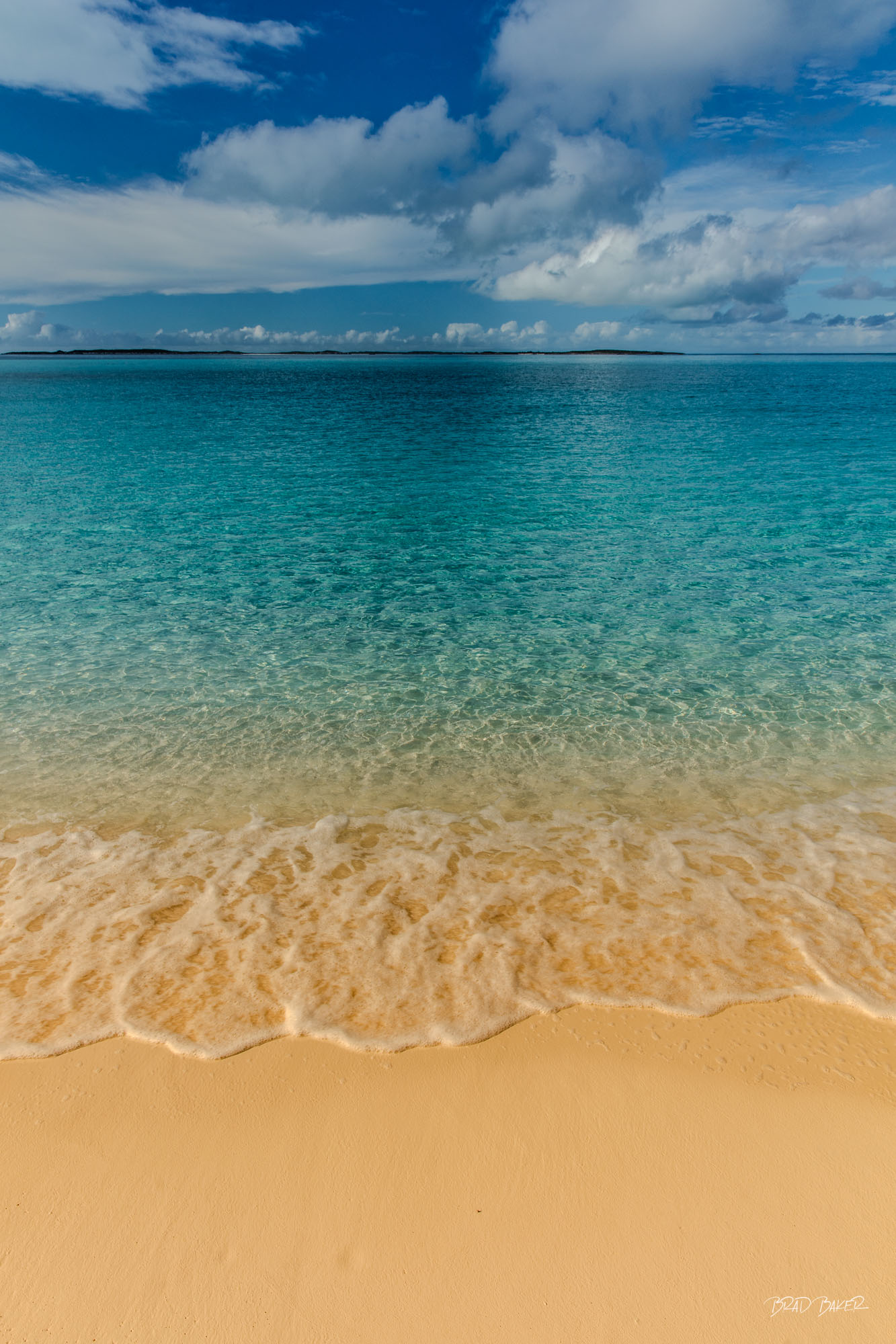 CRYSTAL WATERS Turquoise Bahamas water meeting a sandy beach beneath a dramatic blue sky and clouds