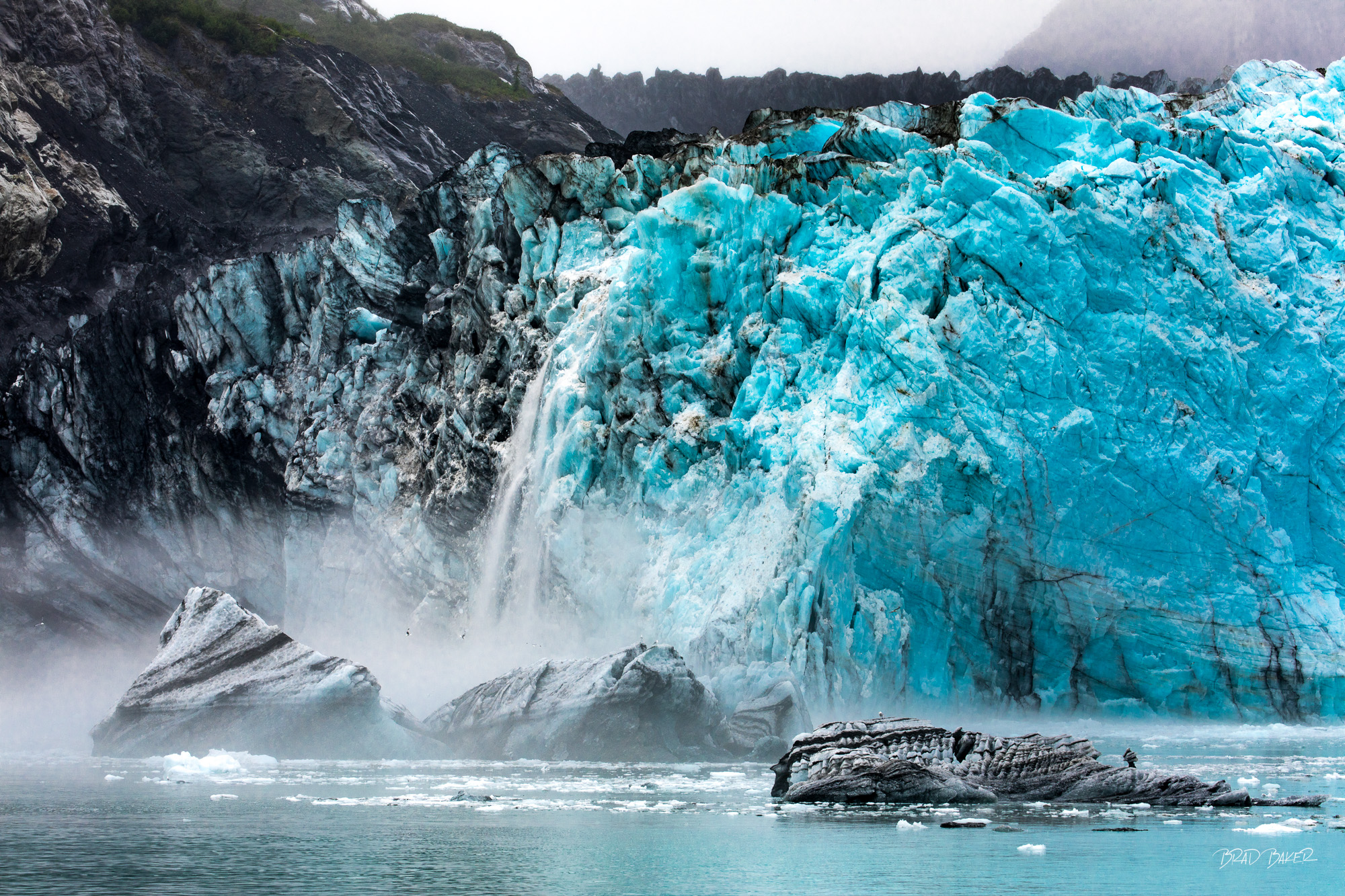 The Turning Point Blue ice calving over a misty fjord with floating pieces of black ice at Margerie Glacier, Glacier Bay National Park Alaska