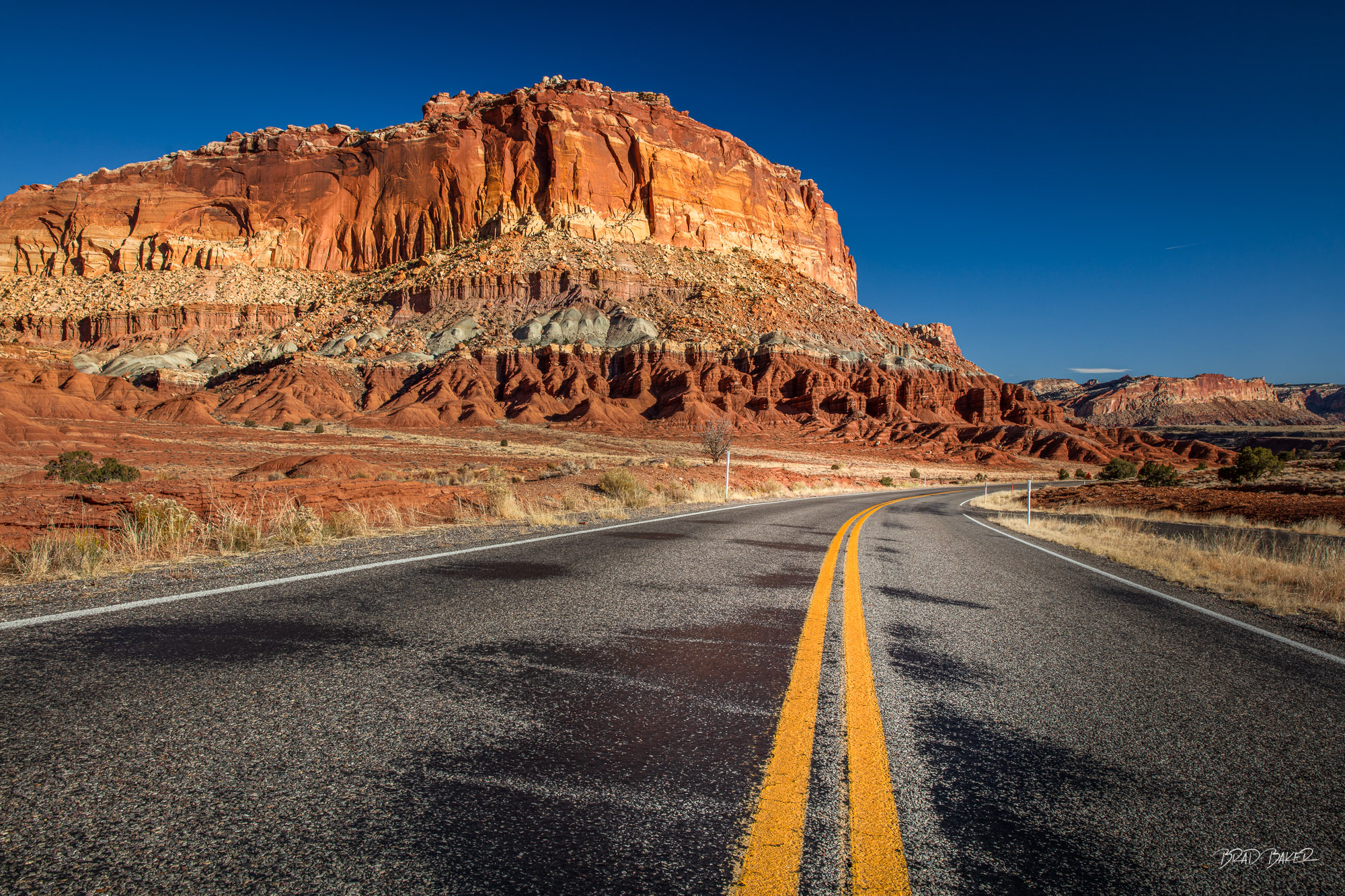 Route 24 Empty two-lane highway leading toward a towering red sandstone butte in Capitol Reef National Park, Utah