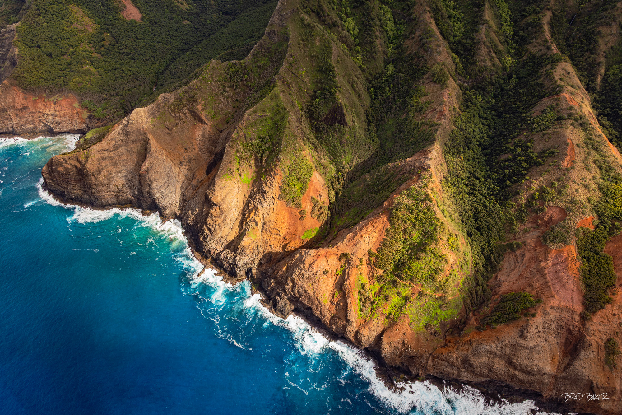 Look Down Doors off Aerial view of rugged orange and green sea cliffs meeting turquoise ocean waves in Kauai, Hawaii.
