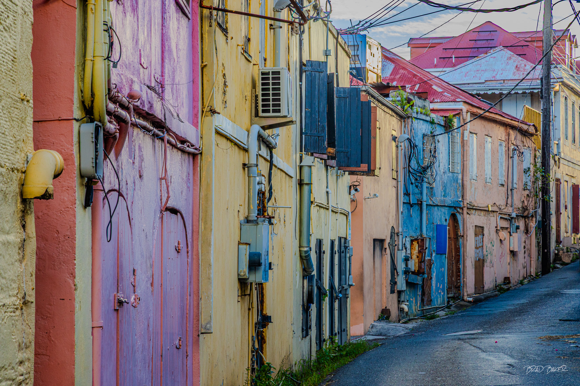 PASTEL ALLEY Narrow Caribbean alley lined with faded pastel-painted historic buildings, pipes, and shuttered doors in soft light in Charlotte Amalie St Thomas USVI