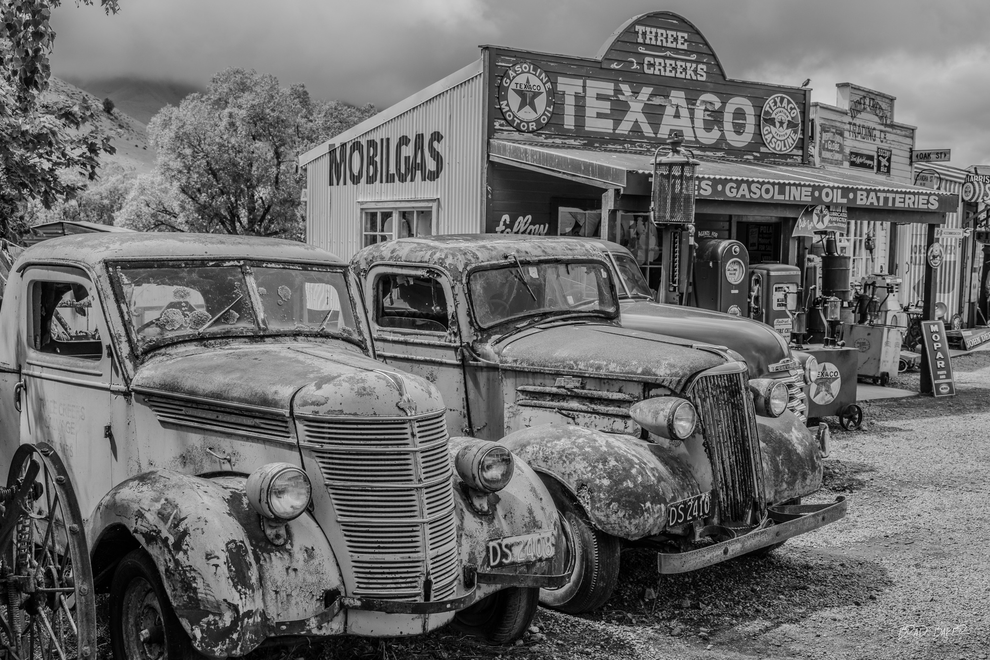 A historic gathering Vintage rusted trucks parked outside retro Texaco and Mobilgas station, black and white, New Zealand