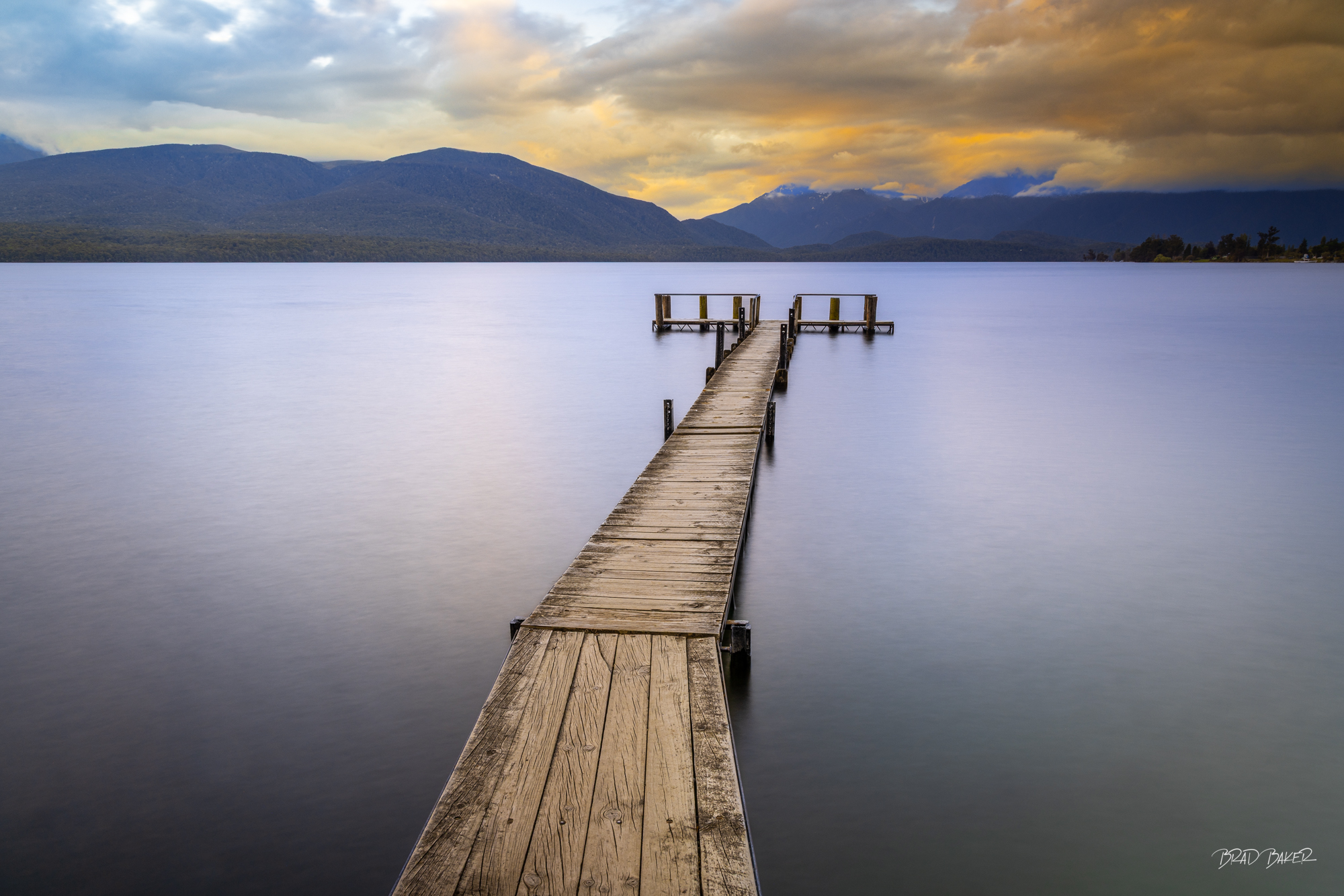 Dead end Dock Long wooden jetty extending into silky smooth lake under dramatic golden cloudscape, Te Anau New Zealand