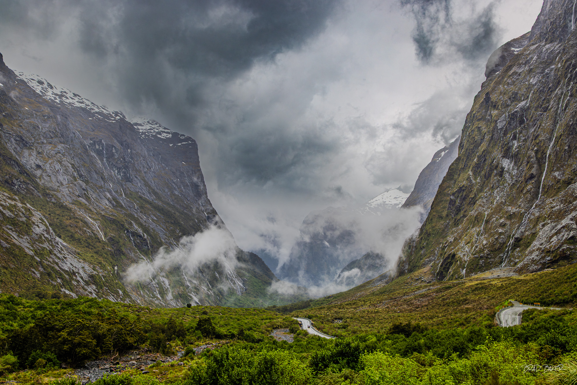 A Hundred Falls Dramatic storm clouds over glacial valley with winding road and cascading waterfalls, Fiordland
