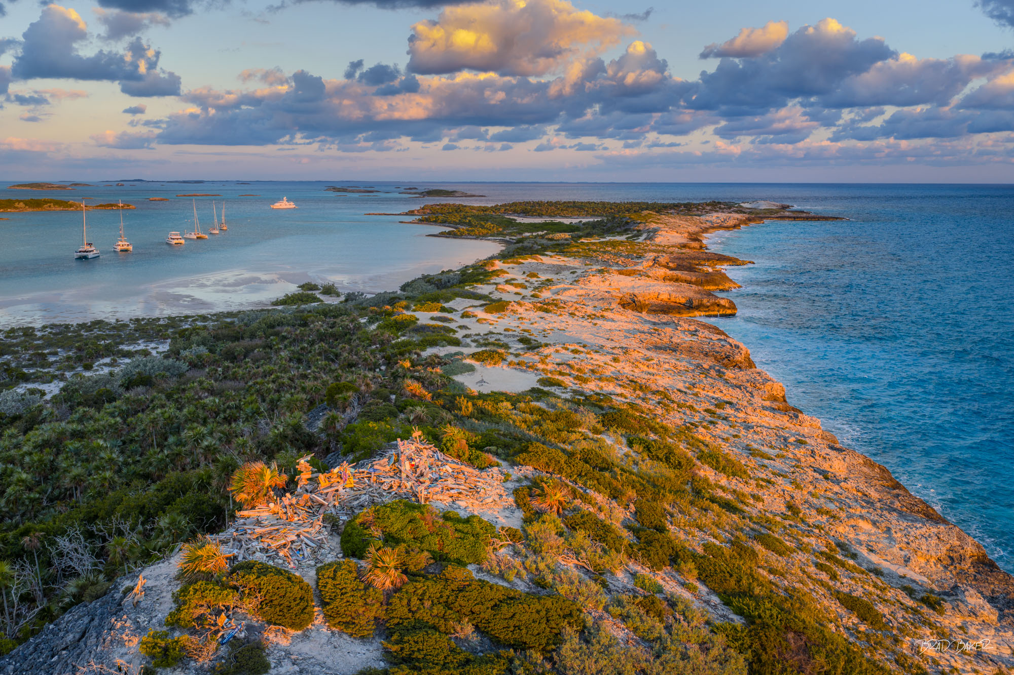 BOO BOO HILL DAWN Sunset view of jagged limestone coastline with sailboats and calm turquoise waters under golden light at Warderick Wells Exumas