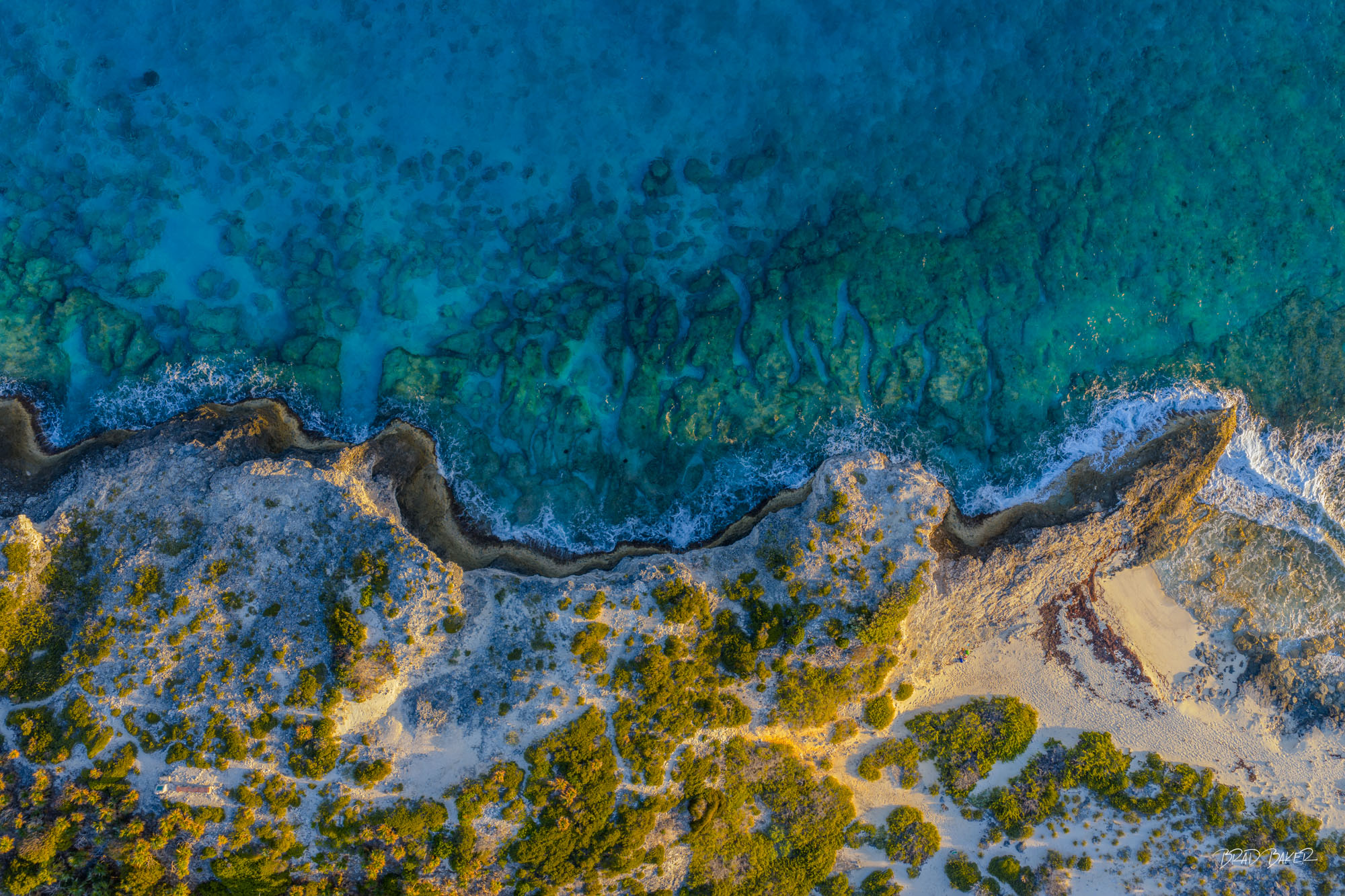 LAND AND SEA Dramatic aerial perspective of rugged coastline meeting turquoise ocean with golden limestone and dense vegetation on The Exumas