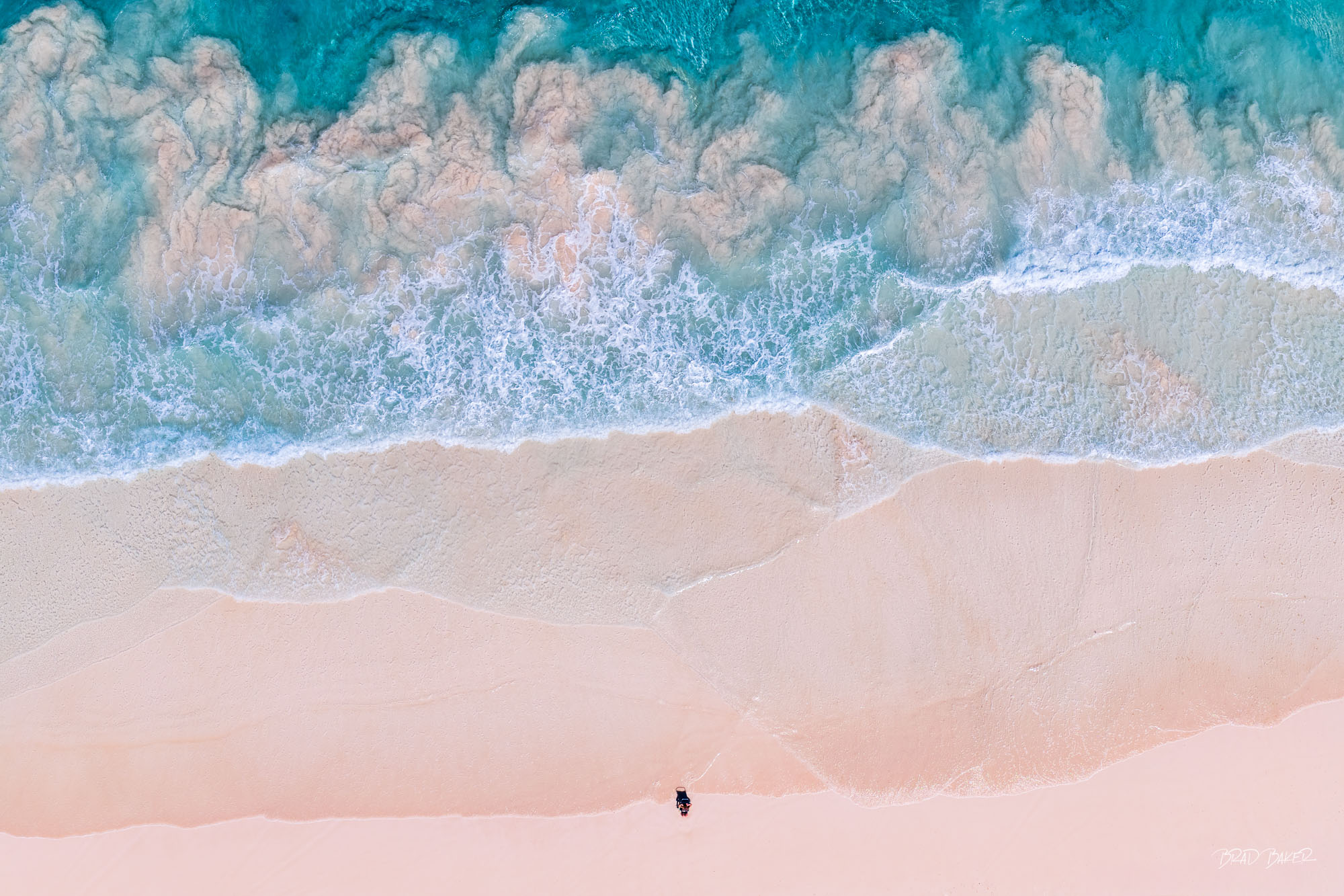THE PERFECT GETAWAY Lone figure rests on a vast pink sand beach as turquoise waves wash ashore from above on Harbor Island Bahamas