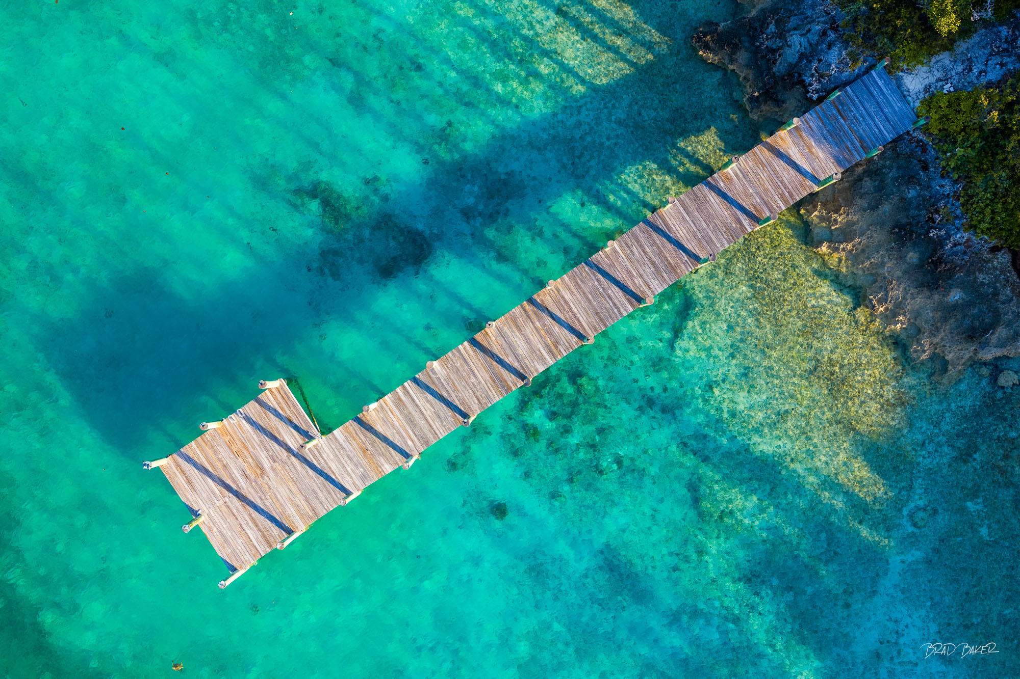 BLUE POLES Aerial view of a wooden dock extending over crystal-clear turquoise water revealing coral formations below in The Bahamas