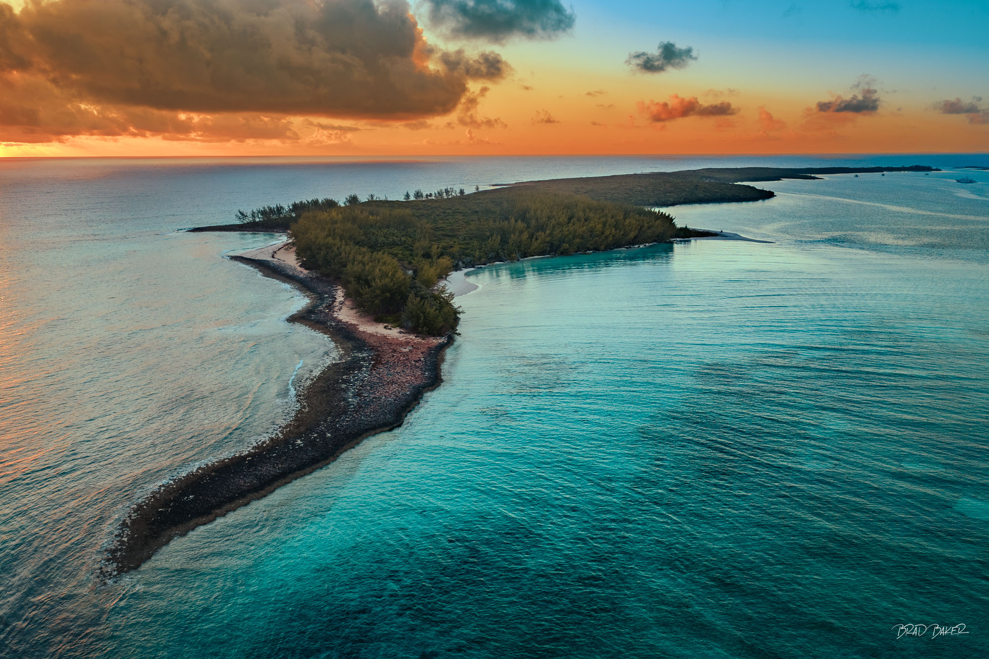 DAWN AT THE DEVIL'S BACKBONE Man island silhouetted against a vibrant orange and blue sunrise over calm Bahamas waters.