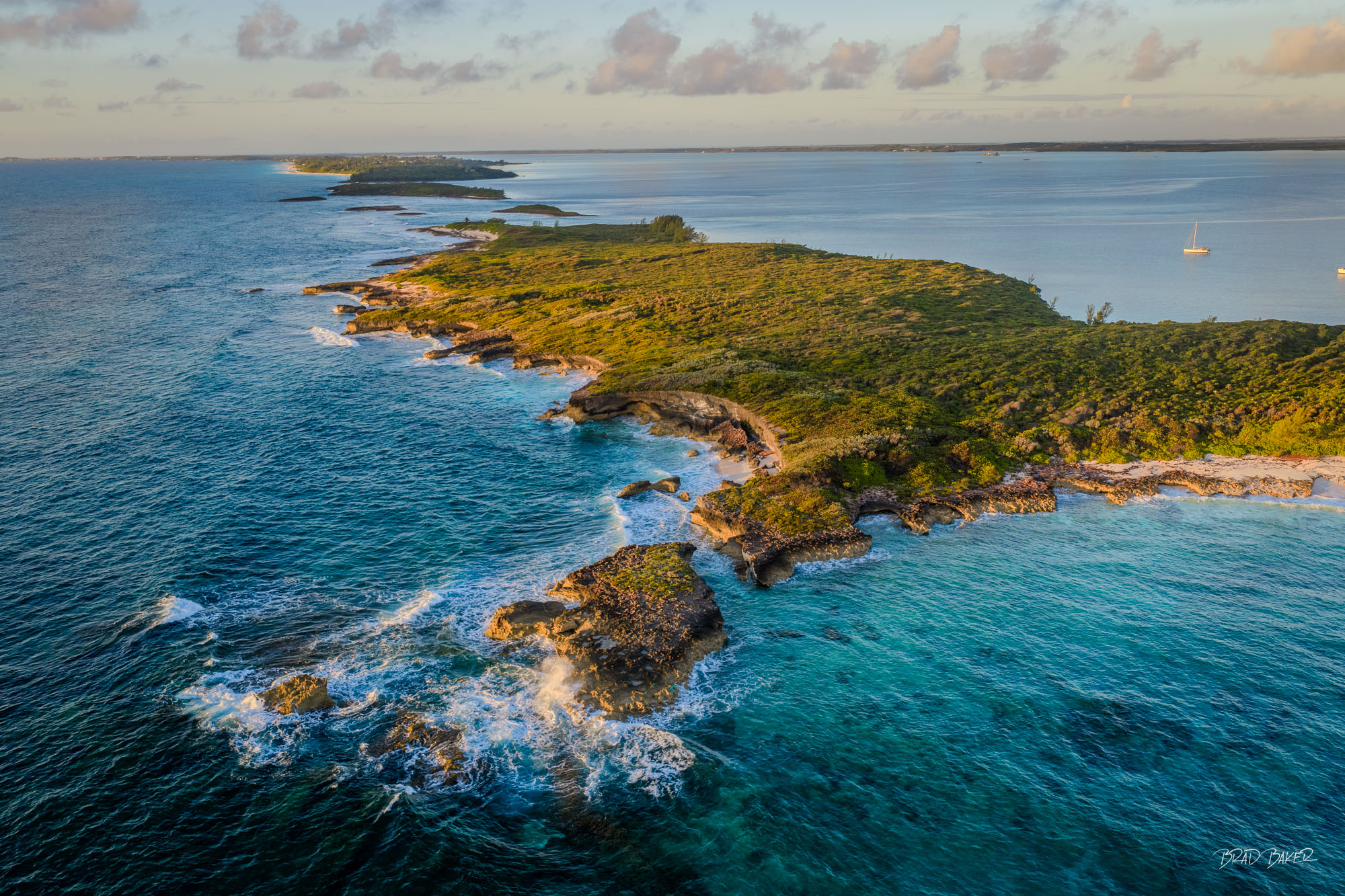 THE EXPOSED SIDE Aerial view of a rugged coral island tip with dense vegetation surrounded by crashing ocean waves in The Bahamas