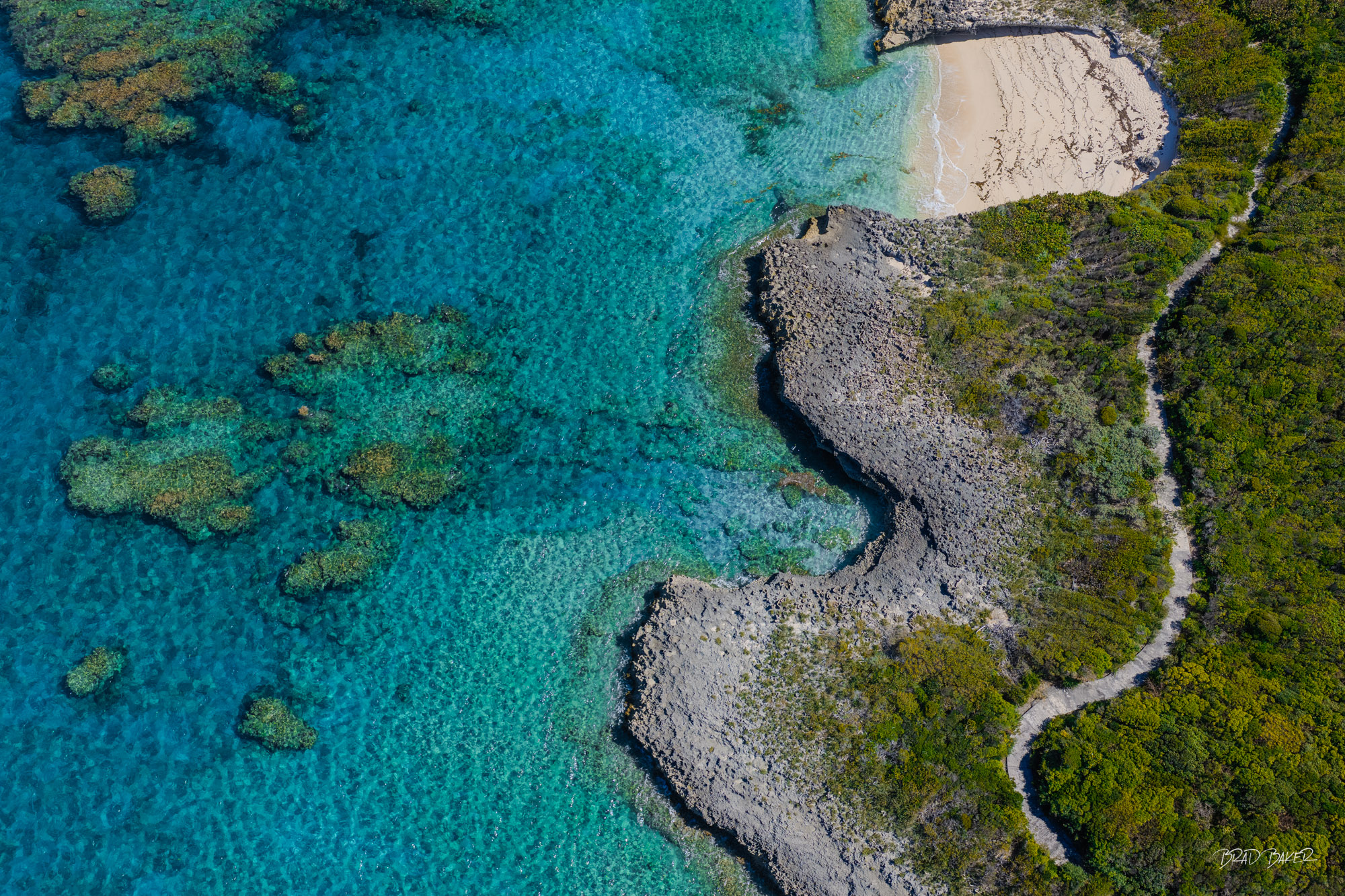 The Winding Path Aerial view of a rugged coral shoreline with a winding path leading to a hidden sandy cove on Harbor Island