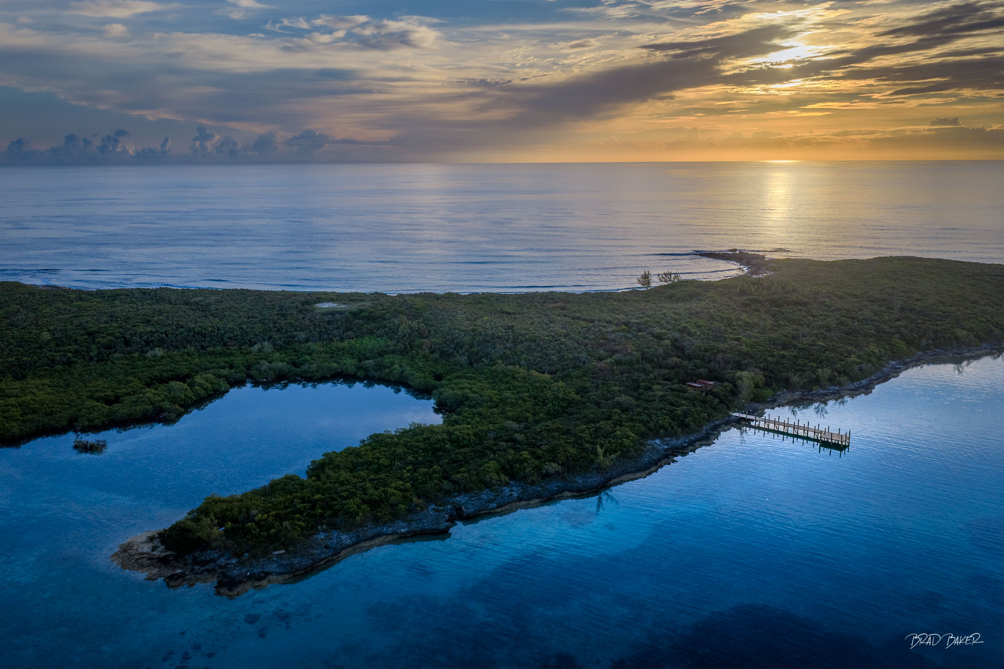 ISLAND BLISS Aerial view of a lush private island at sunrise with a dock, inner bay, and golden horizon in The Bahamas